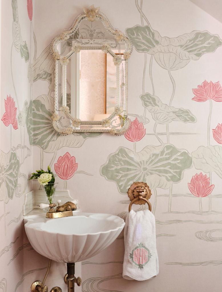 A Venetian-glass mirror, shell-shaped sink, and lovely pink wallpaper transform this tiny under-the-stairs powder bath.
