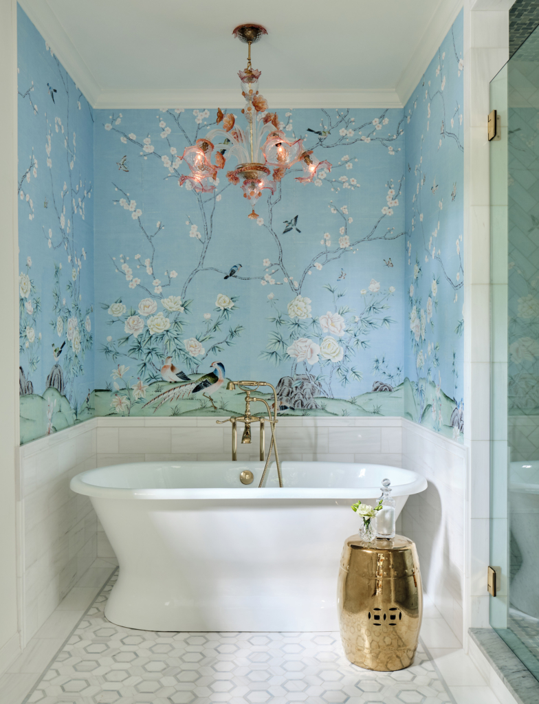 In the primary bath, a chinoiserie-inspired wallpaper with flowers and birds against a pale blue sky turns this tub niche into a calming oasis.