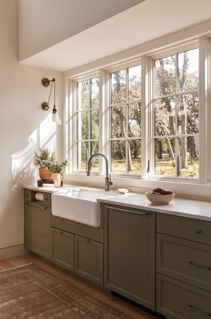 Olive green kitchen cabinets paired with walls in Sherwin-Williams "Alabaster", with natural light streaming in from the side window.