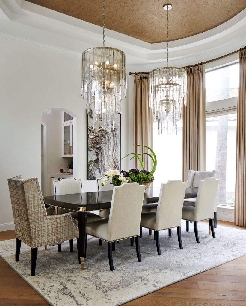 Dining room with a touch of luxury with the dual chandeliers and the wallpapered ceiling.