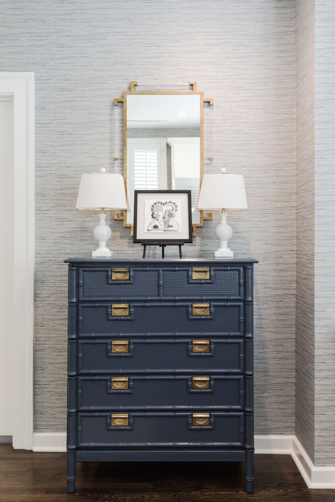 A navy blue console with a blue linen-look grasscloth wallpaper backdrop in the guest living area.