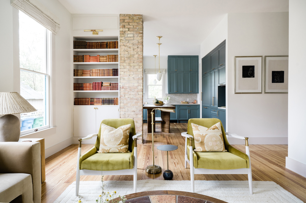 This inviting living room features elegant green chairs with a view into a blue-accented kitchen. Walls painted in Farrow & Ball "All White".